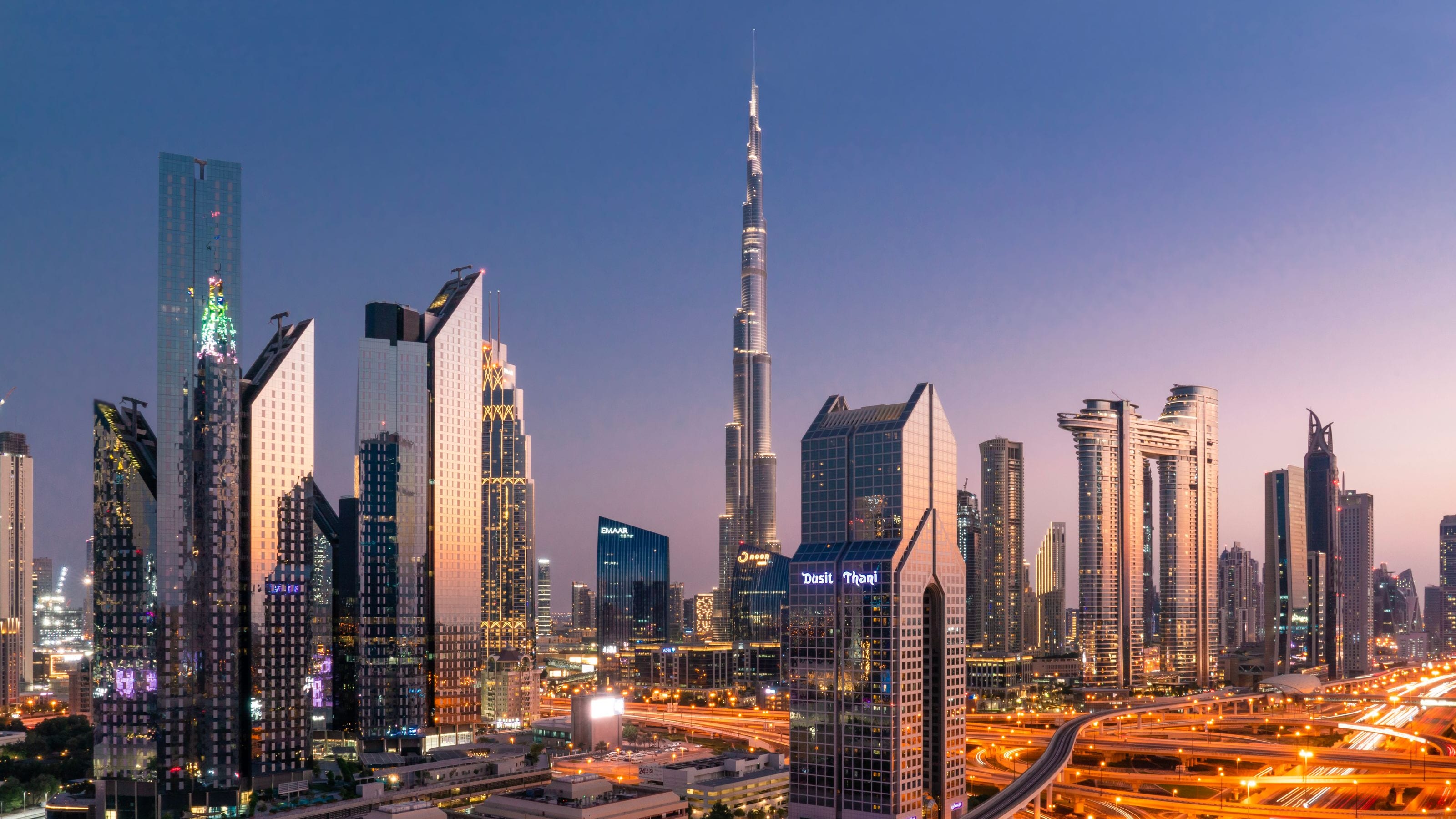 Downtown Dubai at dusk, Burj Khalifa rising over the towers of Sheikh Zayed Road and the light trails of the interchange below