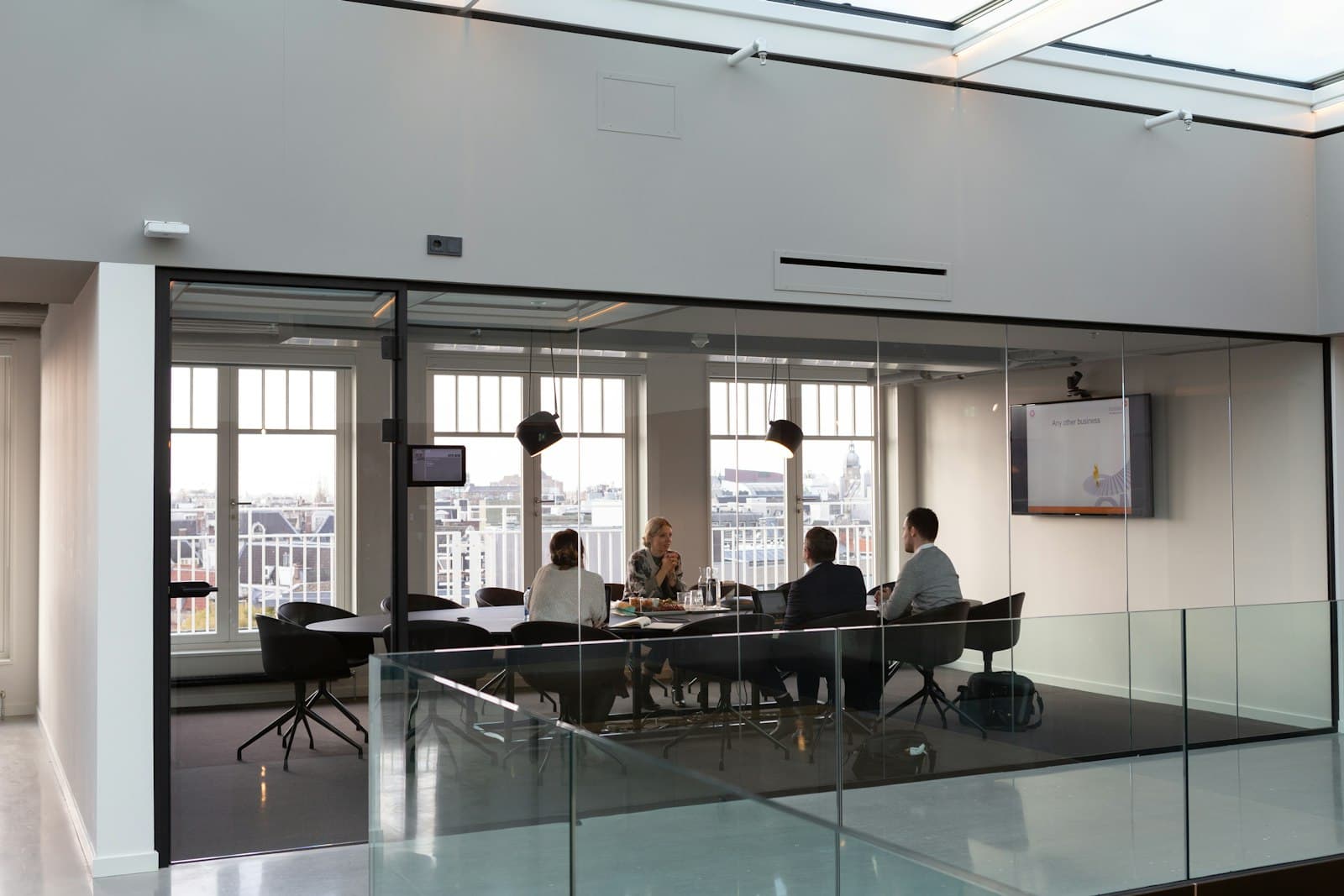 Four colleagues meeting around the table of a glass-walled boardroom, with files open in front of them